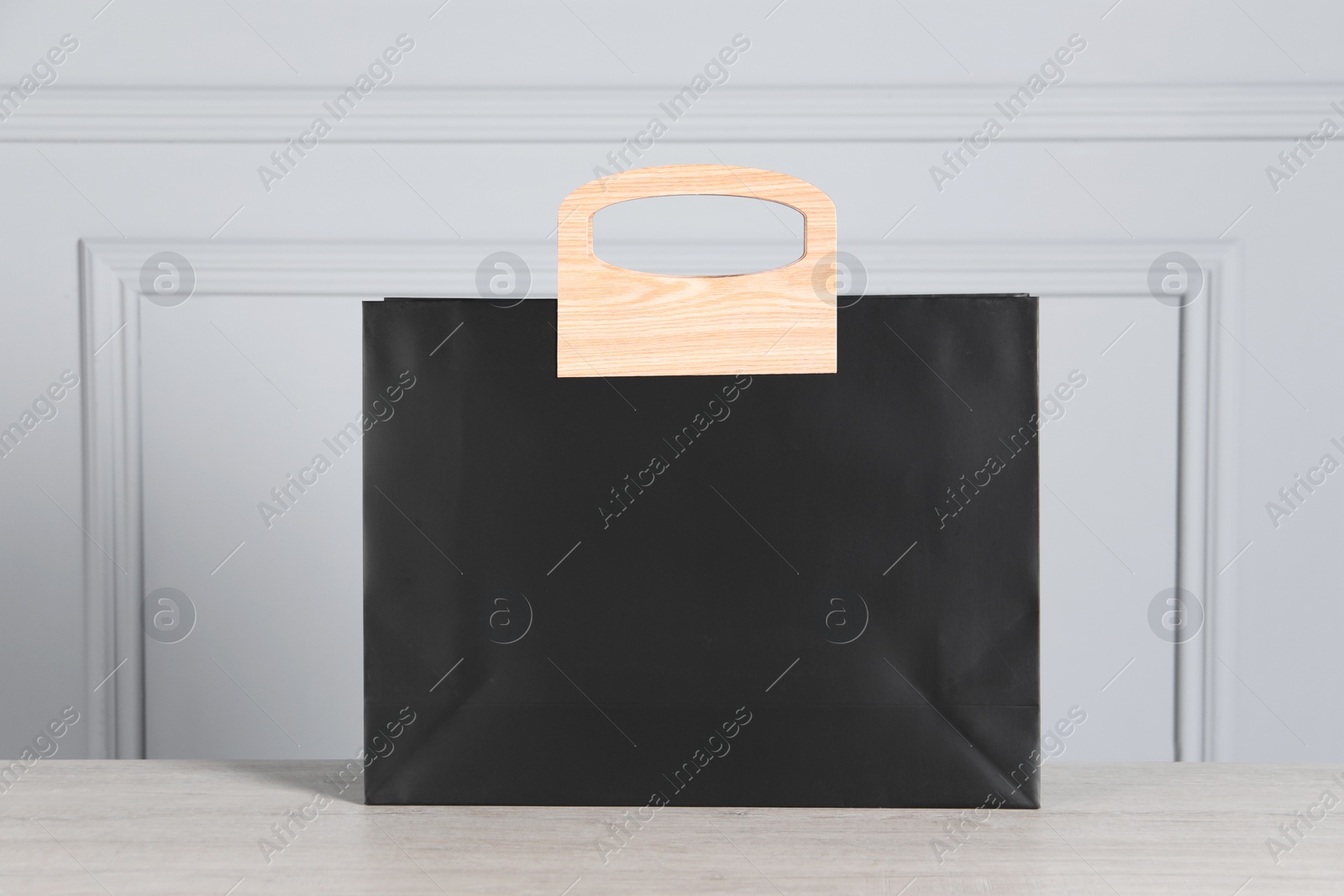 Photo of Black paper bag on wooden table against light grey wall