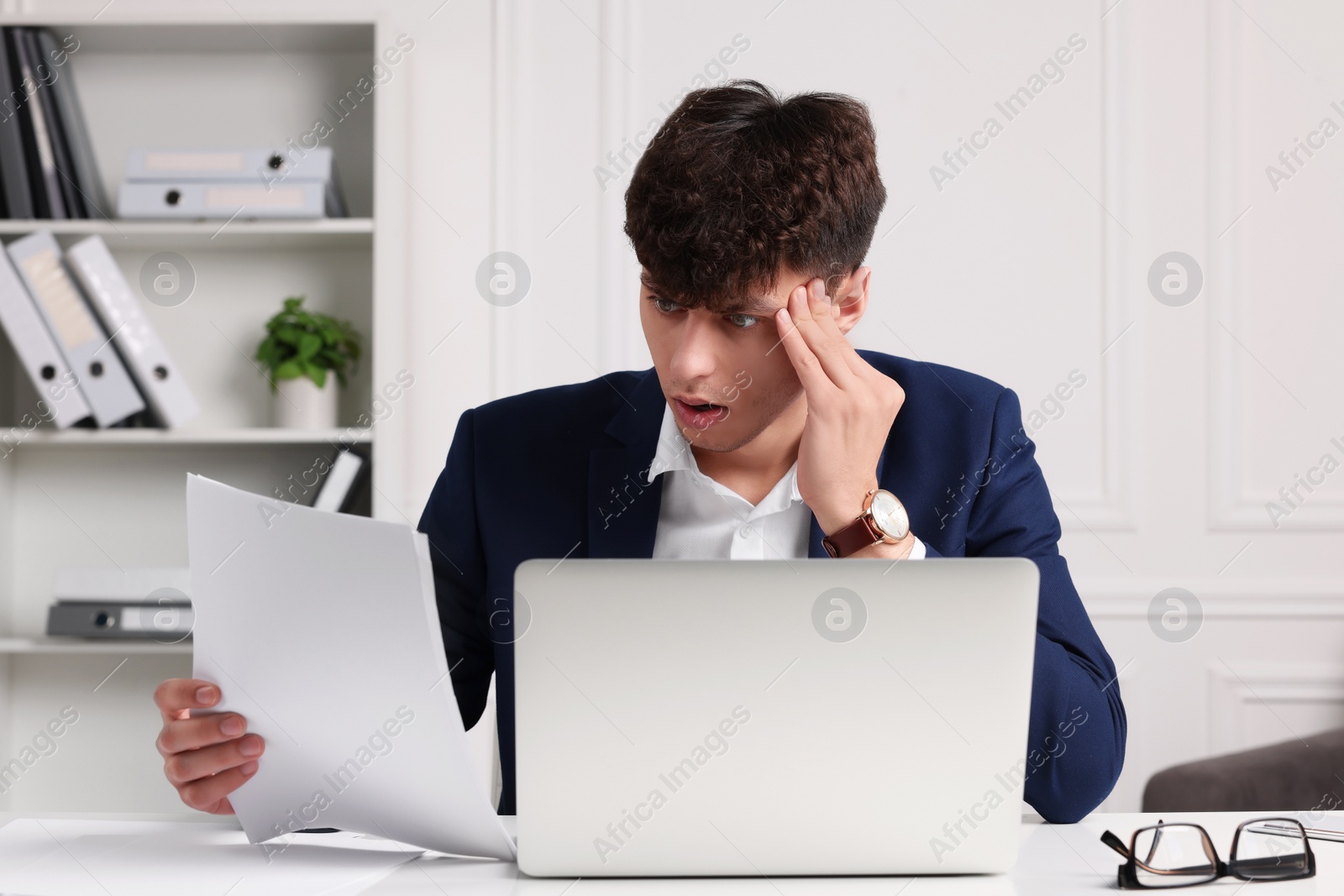 Photo of Emotional young man working at white table in office. Deadline concept