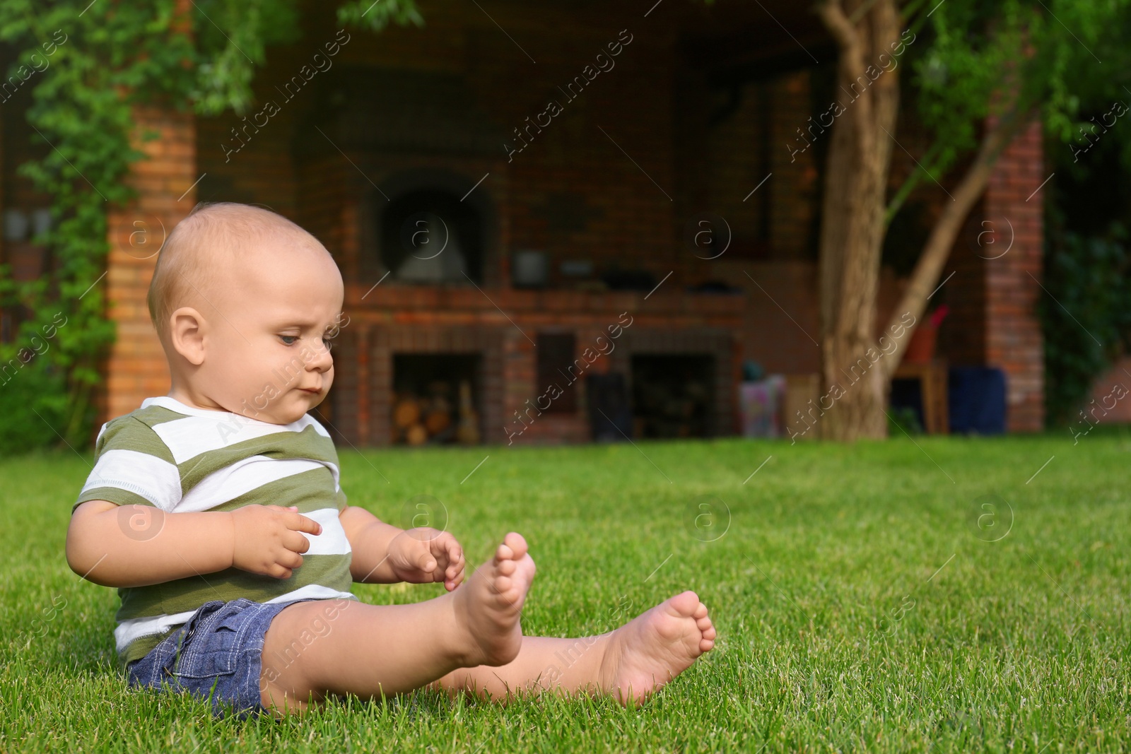 Photo of Adorable little baby sitting on green grass outdoors