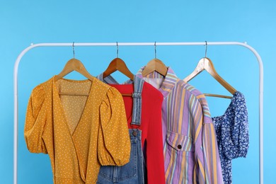 Photo of Rack with stylish women`s clothes on wooden hangers against light blue background