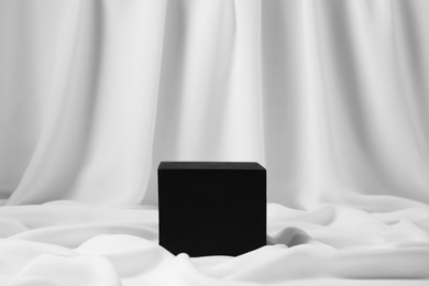 Photo of Black cube on white fabric. Stylish presentation for product