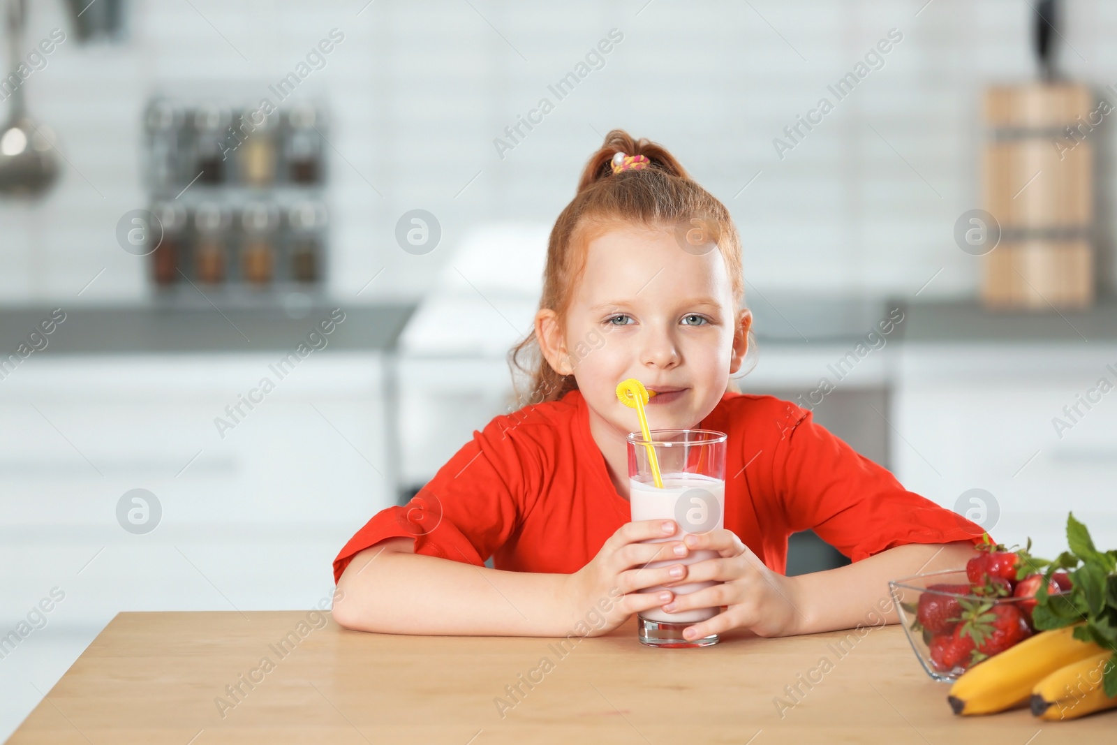 Photo of Little girl with glass of delicious milk shake in kitchen