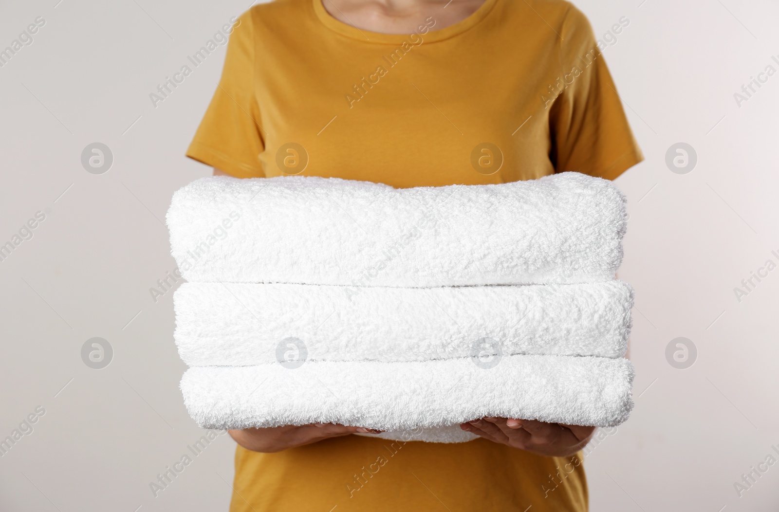 Photo of Woman holding fresh towels on light background, closeup