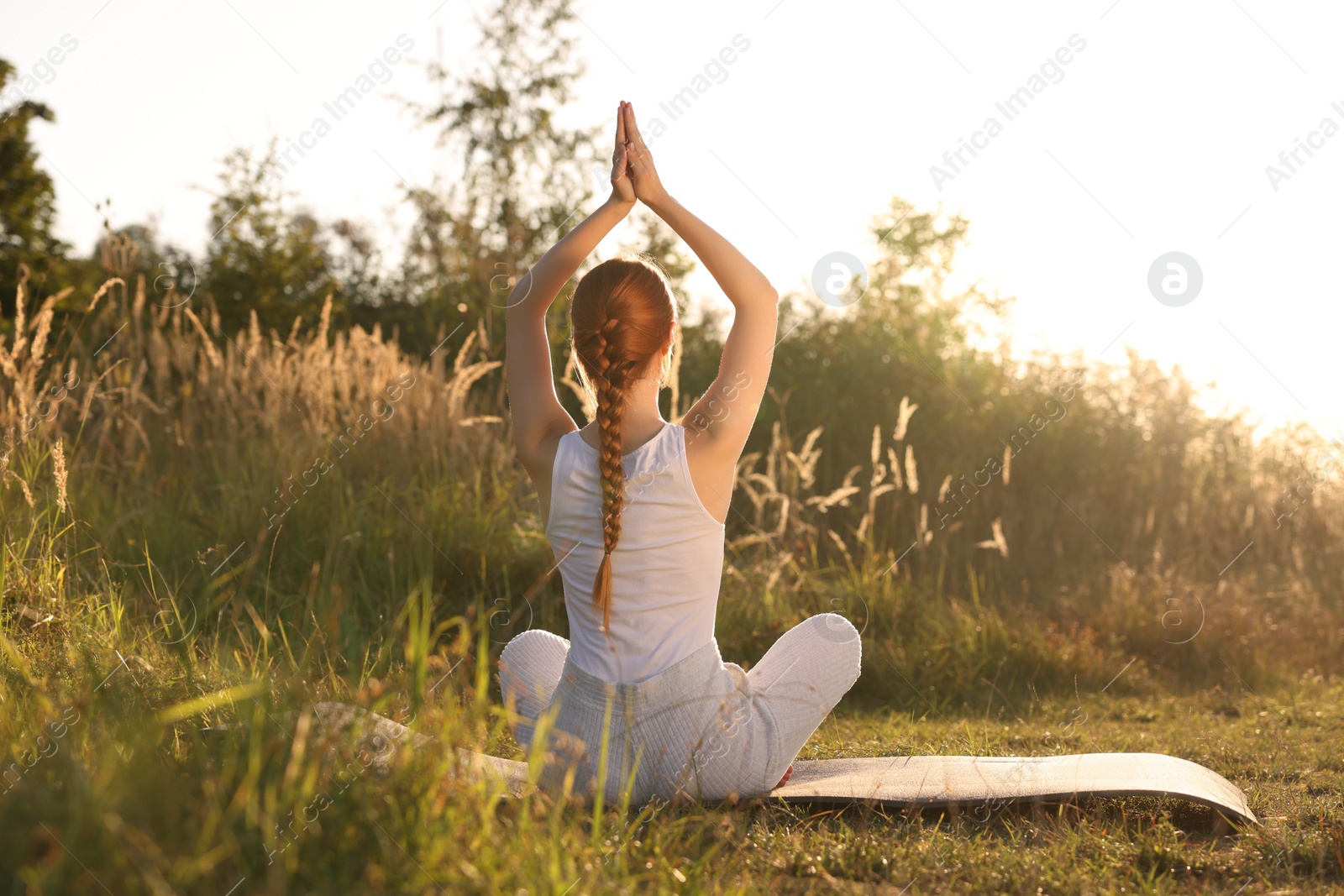 Photo of Woman practicing Padmasana on yoga mat outdoors on sunny day, back view. Lotus pose