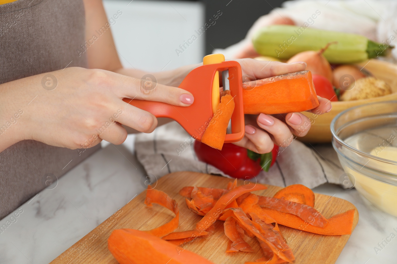 Photo of Woman peeling fresh carrot at white marble table, closeup