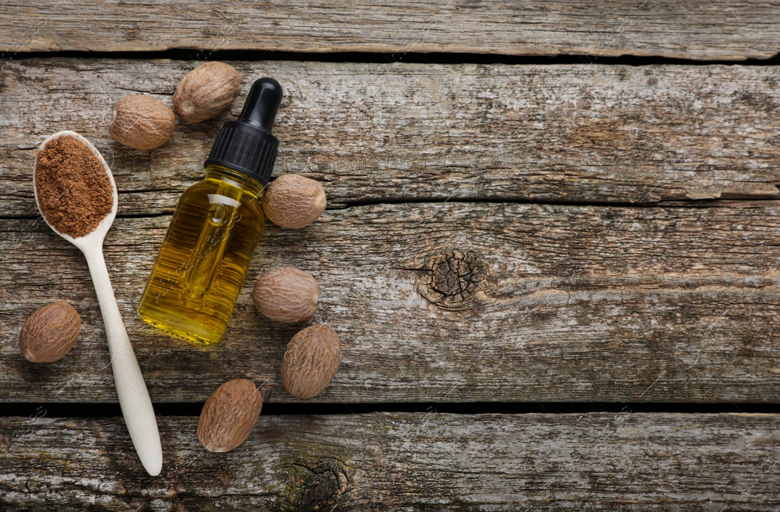 Photo of Bottle of nutmeg oil, nuts and powder on wooden table, flat lay. Space for text