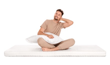 Photo of Smiling man with pillow sitting on soft mattress against white background