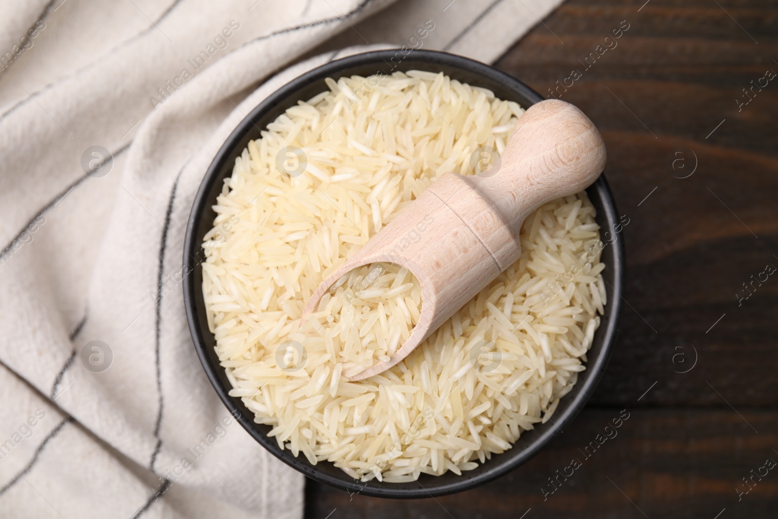 Photo of Bowl and scoop with raw rice on wooden table, top view