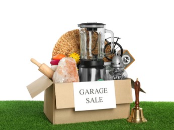 Photo of Box with sign Garage Sale and different stuff on green grass against white background