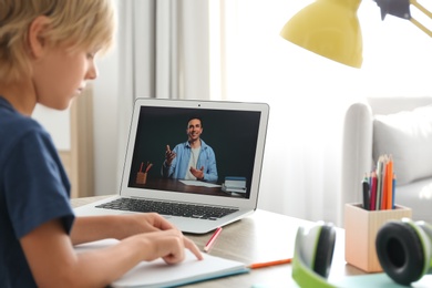 Photo of Little boy studying with teacher via video conference at home. Distance learning during COVID-19 pandemic