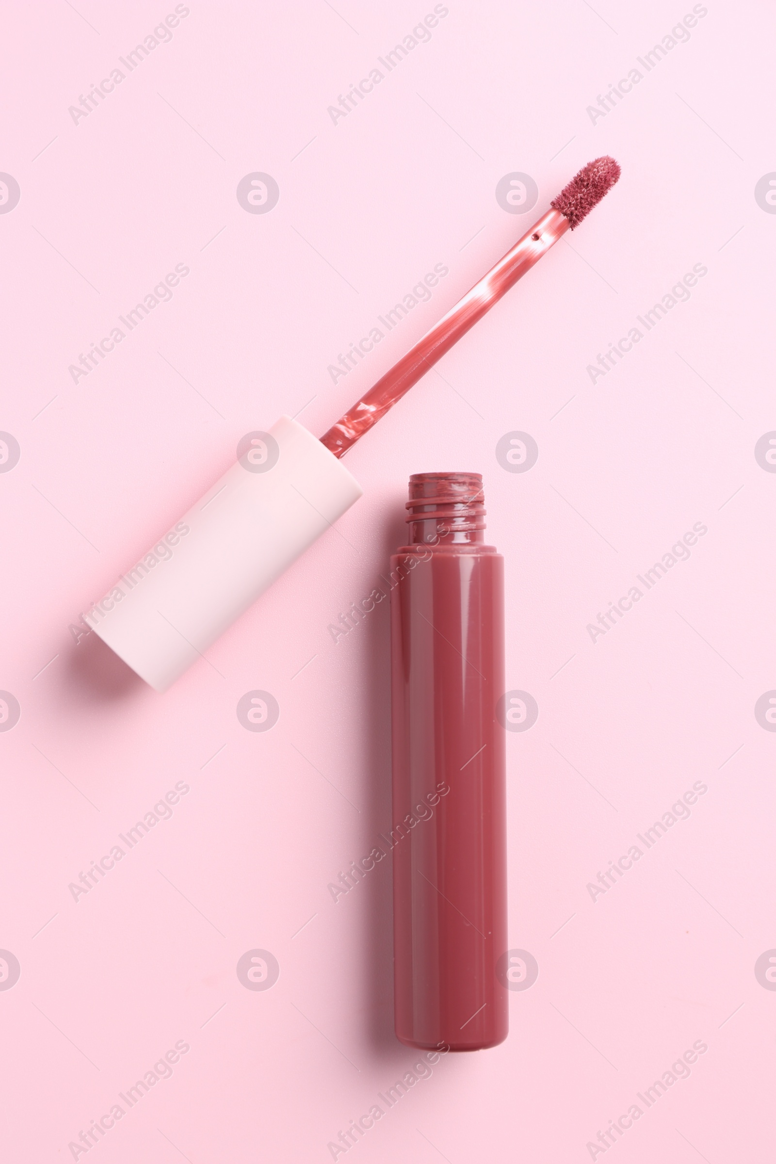 Photo of Bright lip gloss and applicator on pink background, top view