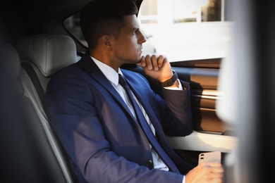 Photo of Handsome man with smartphone on backseat of modern car