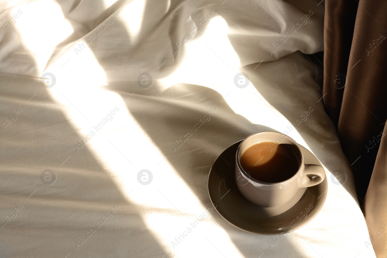 Photo of Cup of aromatic coffee on bed in morning, space for text