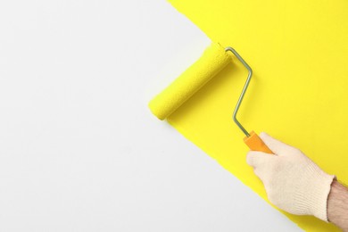 Photo of Man applying orange paint with roller brush on white wall, closeup