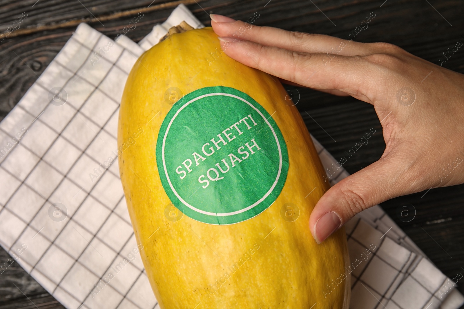 Photo of Woman holding ripe spaghetti squash on dark table, top view