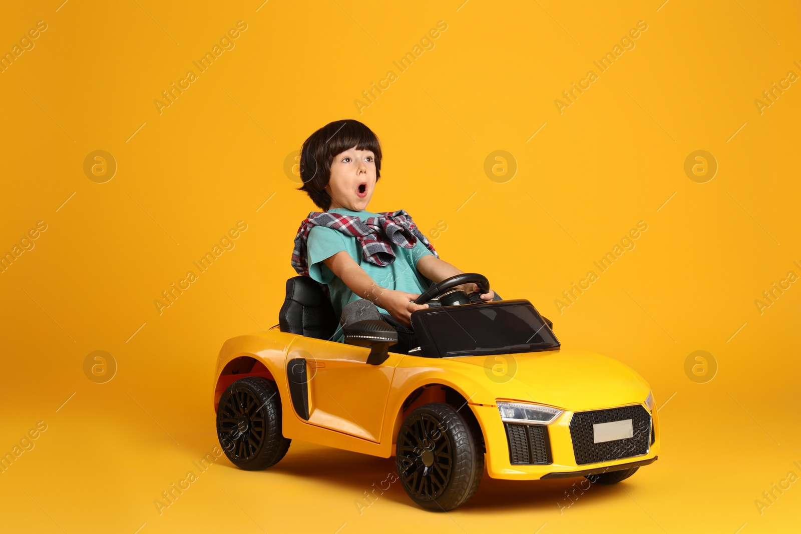 Photo of Little child driving toy car on yellow background