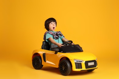 Little child driving toy car on yellow background