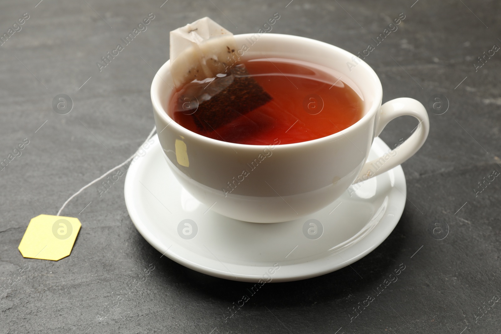 Photo of Tea bag in cup with hot drink on grey textured table, closeup