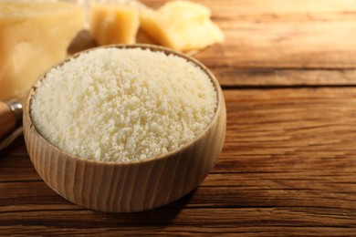 Photo of Bowl with grated parmesan cheese on wooden table, closeup. Space for text