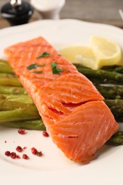 Photo of Tasty grilled salmon with asparagus and lemon on plate, closeup