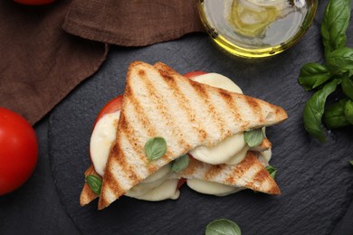 Photo of Delicious grilled sandwiches with mozzarella, tomatoes and basil on black table, flat lay