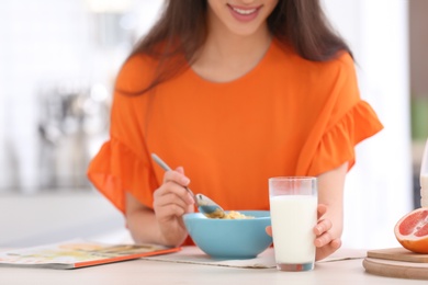 Beautiful young woman having breakfast and drinking milk at table