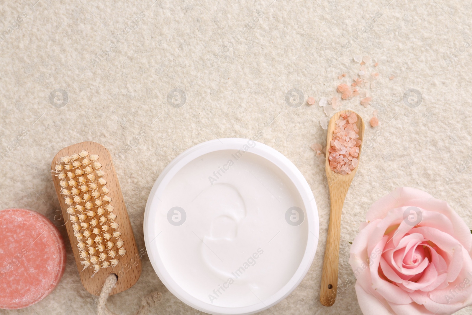 Photo of Flat lay composition with moisturizing cream in open jar and other body care products on light textured table