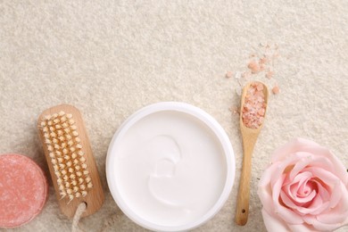 Photo of Flat lay composition with moisturizing cream in open jar and other body care products on light textured table