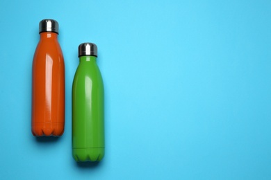 Photo of Modern thermo bottles on light blue background, flat lay. Space for text