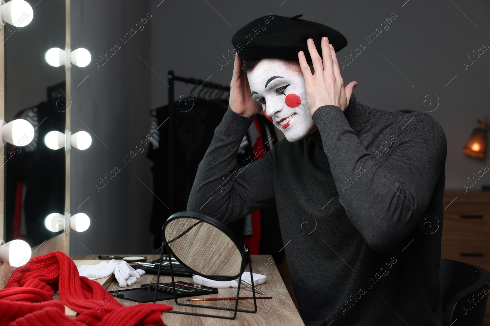 Photo of Mime artist putting on beret near mirror in dressing room