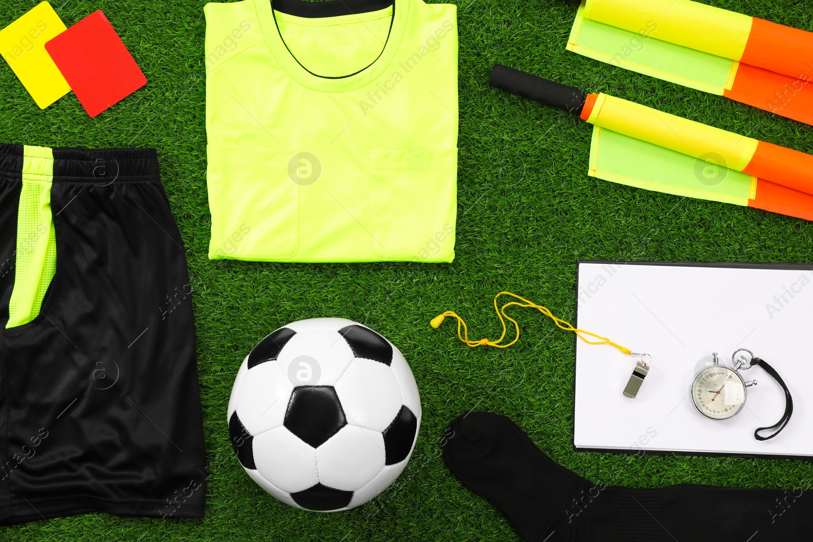 Photo of Uniform, soccer ball and other referee equipment on green grass, flat lay