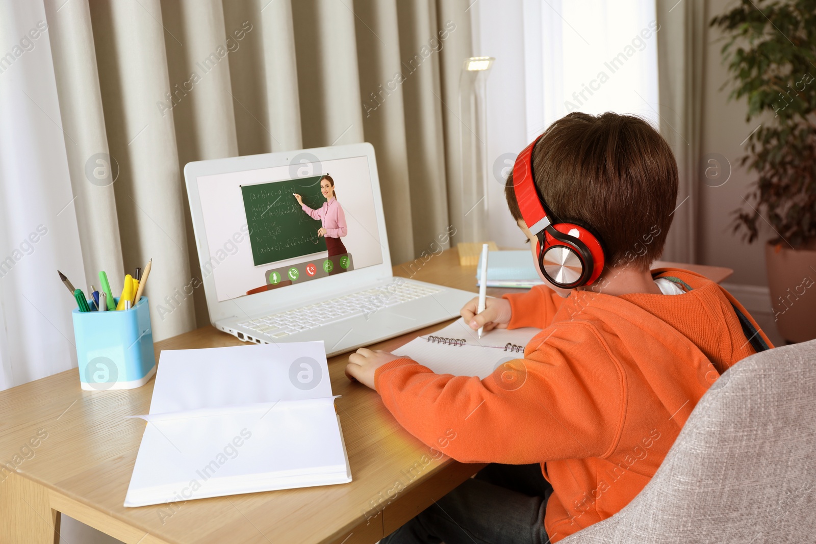 Image of E-learning. Little boy taking notes during online lesson at wooden table indoors