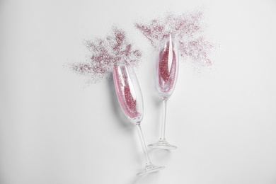 Photo of Champagne glasses with pink glitter on white background, top view. Hilarious celebration