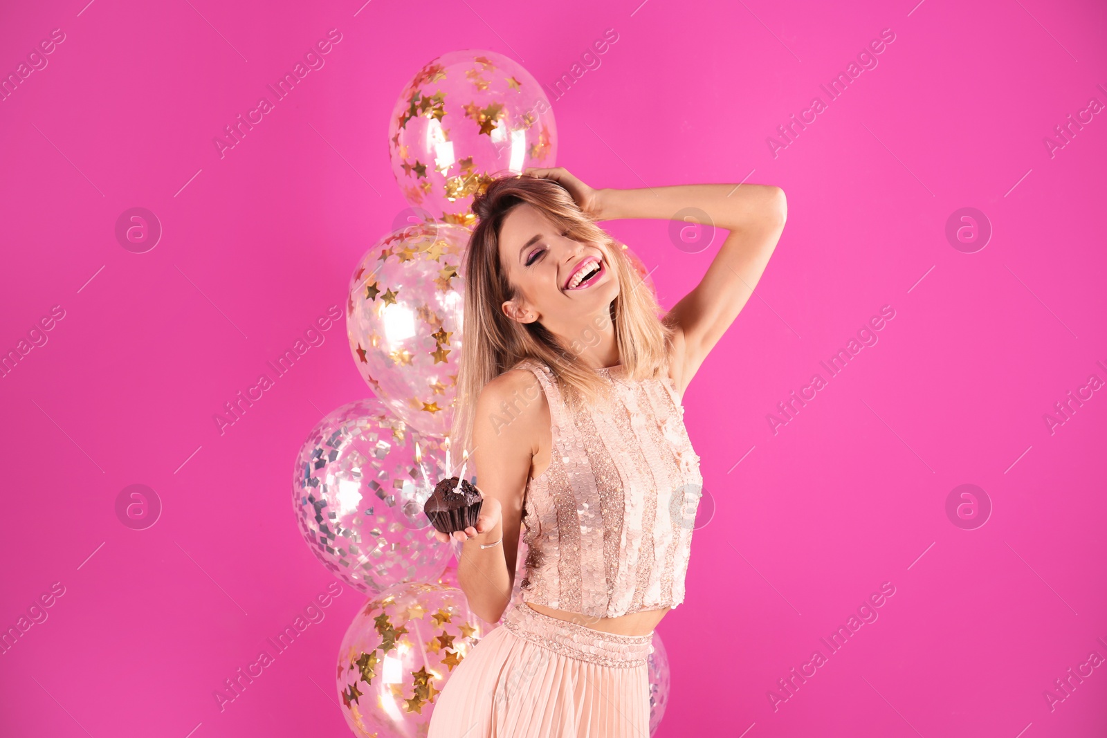 Photo of Young woman with birthday muffin and air balloons on color background