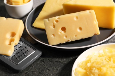 Photo of Grated, whole pieces of cheese and grater on dark textured table, closeup