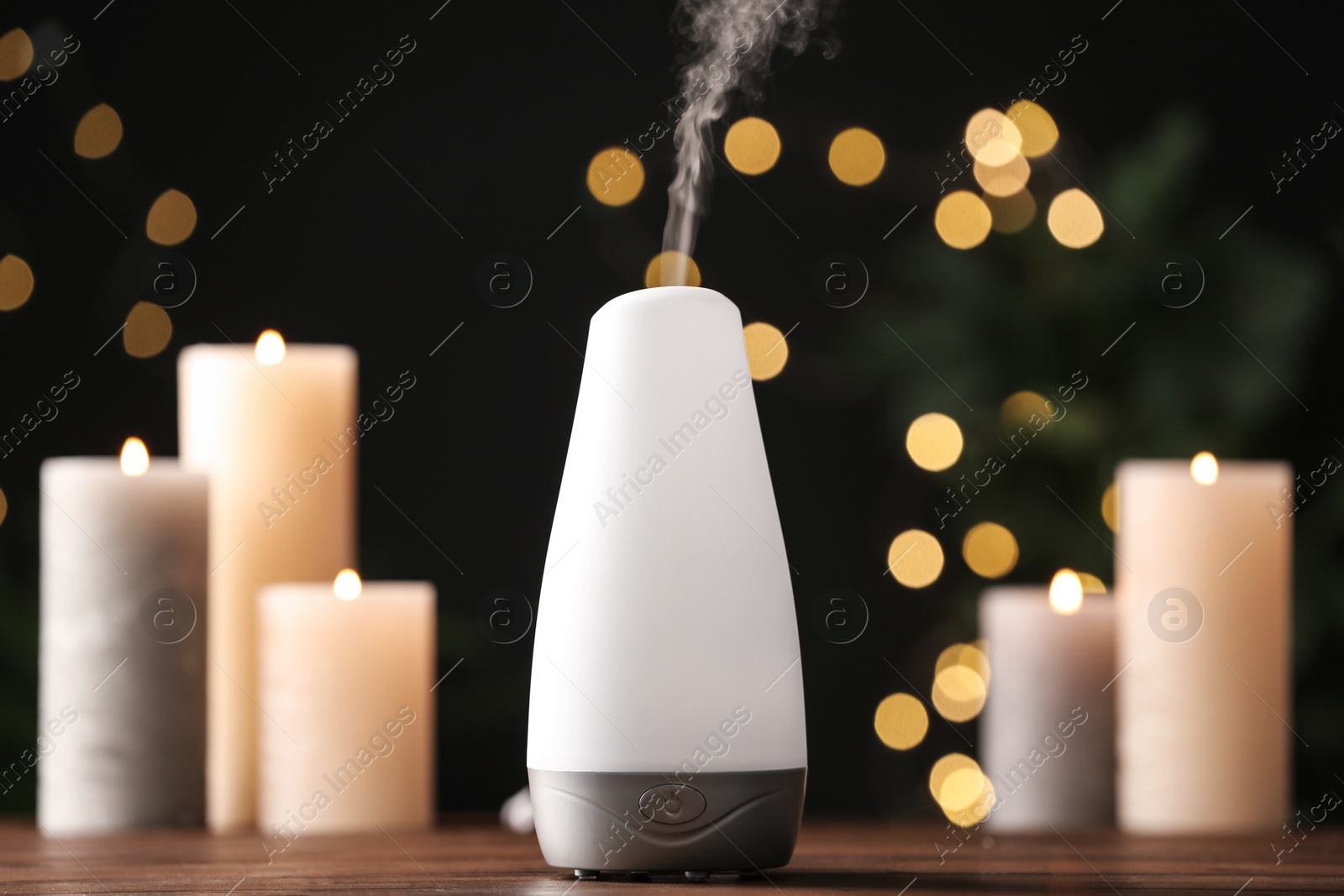 Photo of Modern aroma humidifier with candles on wooden table against blurred lights, space for text