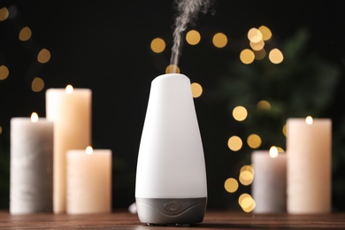 Photo of Modern aroma humidifier with candles on wooden table against blurred lights, space for text