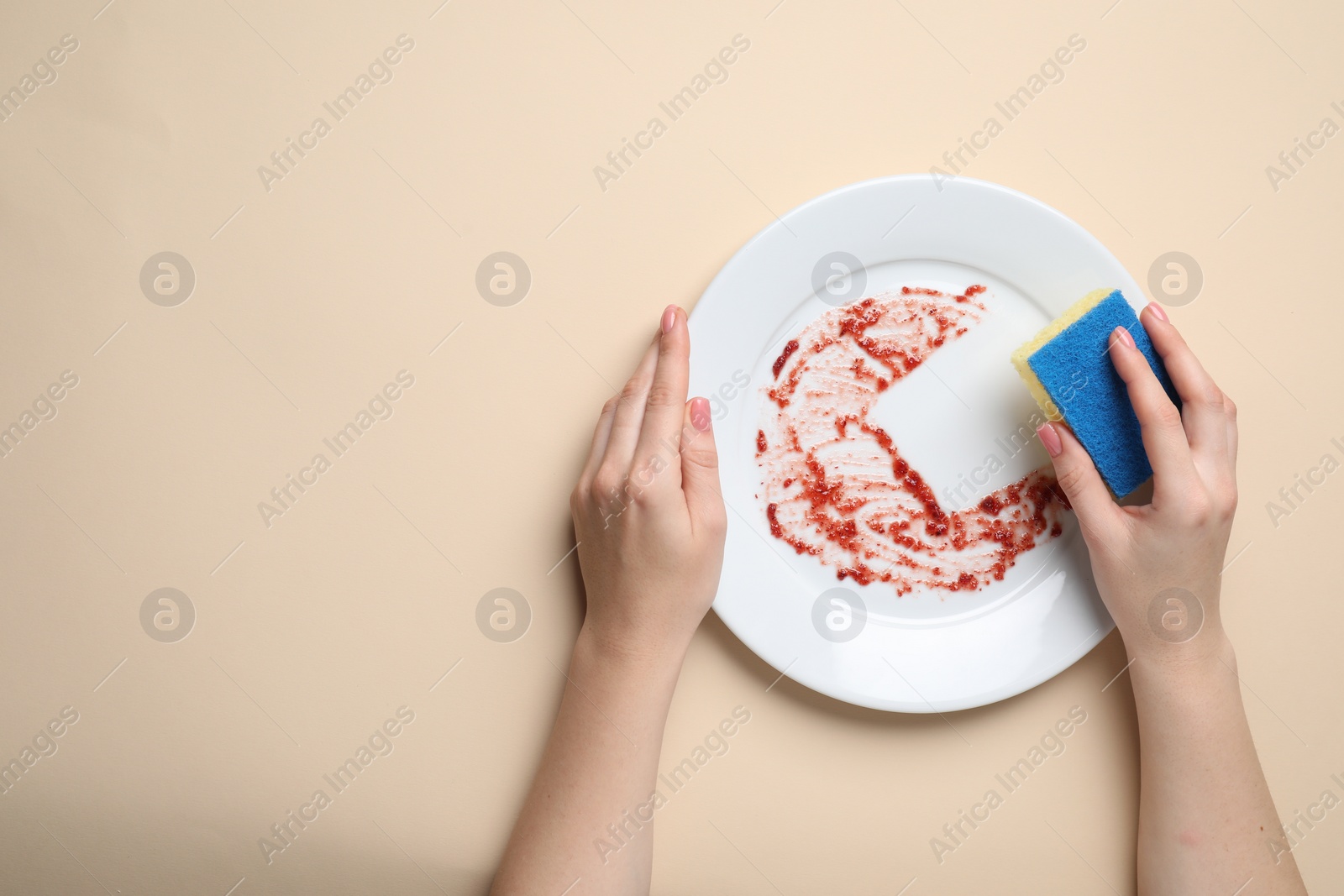 Photo of Woman washing dirty plate with sponge on beige background, top view. Space for text