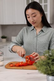Photo of Cooking process. Beautiful woman cutting bell pepper at white countertop in kitchen