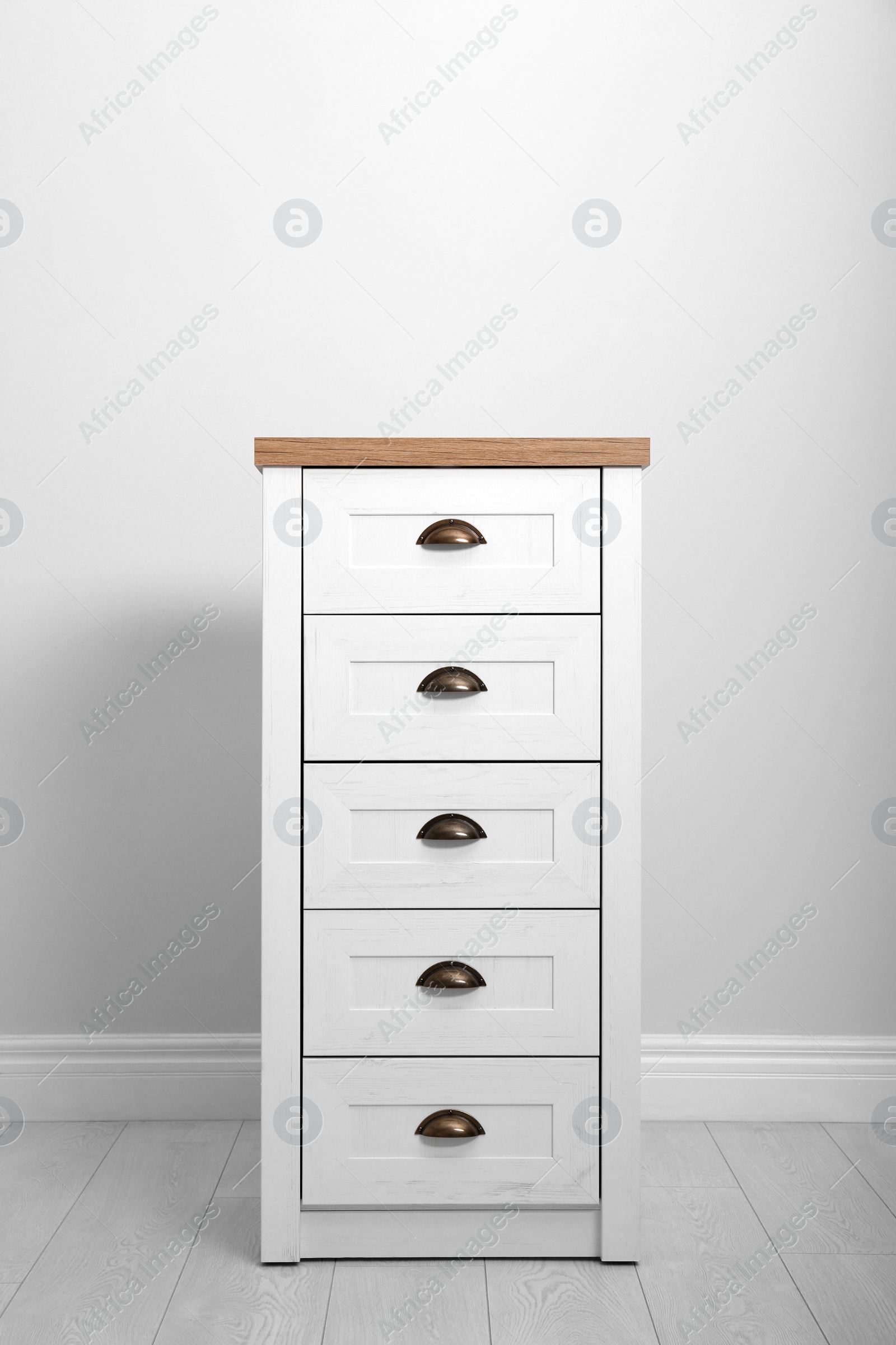 Photo of Stylish chest of drawers near white wall. Furniture for wardrobe room