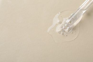 Pipette with cosmetic serum on beige background, macro view. Space for text