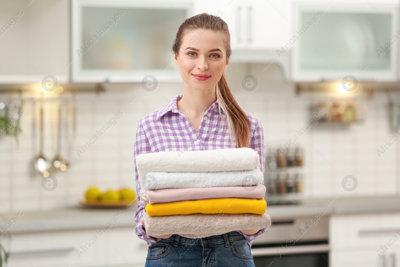 Photo of Woman holding folded clean towels in kitchen. Laundry day