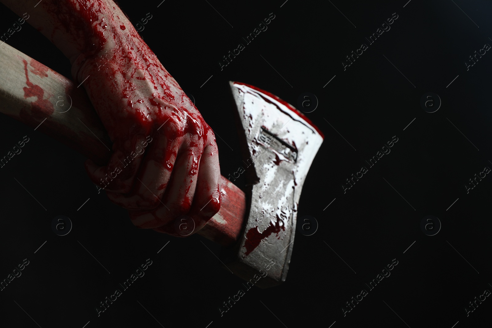 Photo of Man holding bloody axe on black background, closeup. Space for text