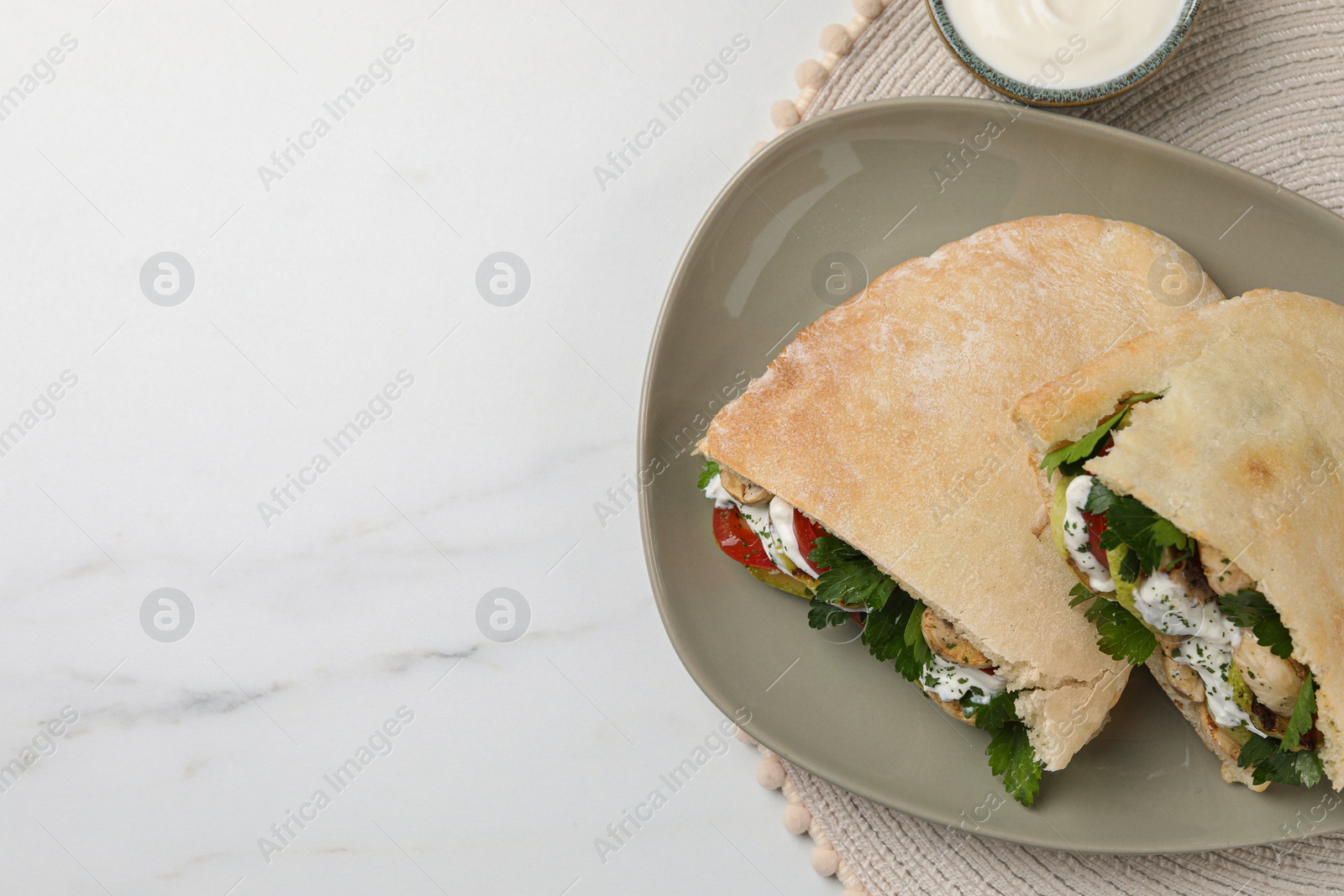 Photo of Delicious pita sandwiches with grilled vegetables and sour cream sauce on white marble table, flat lay. Space for text