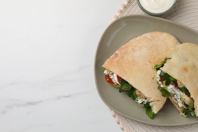 Delicious pita sandwiches with grilled vegetables and sour cream sauce on white marble table, flat lay. Space for text