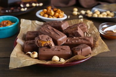 Photo of Many tasty chocolate bars and nuts on wooden table, closeup