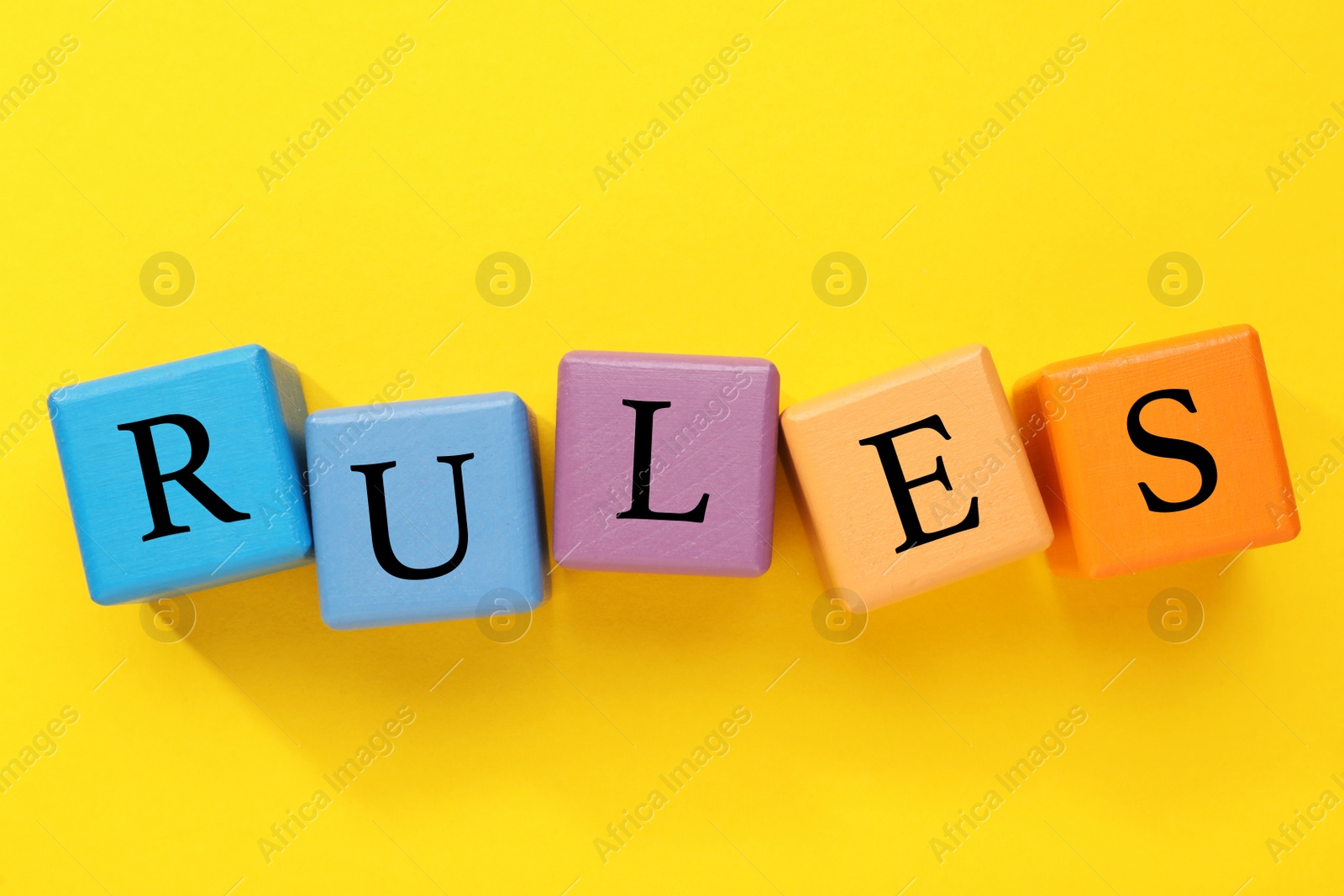 Photo of Word Rules made of colorful cubes with letters on yellow background, flat lay