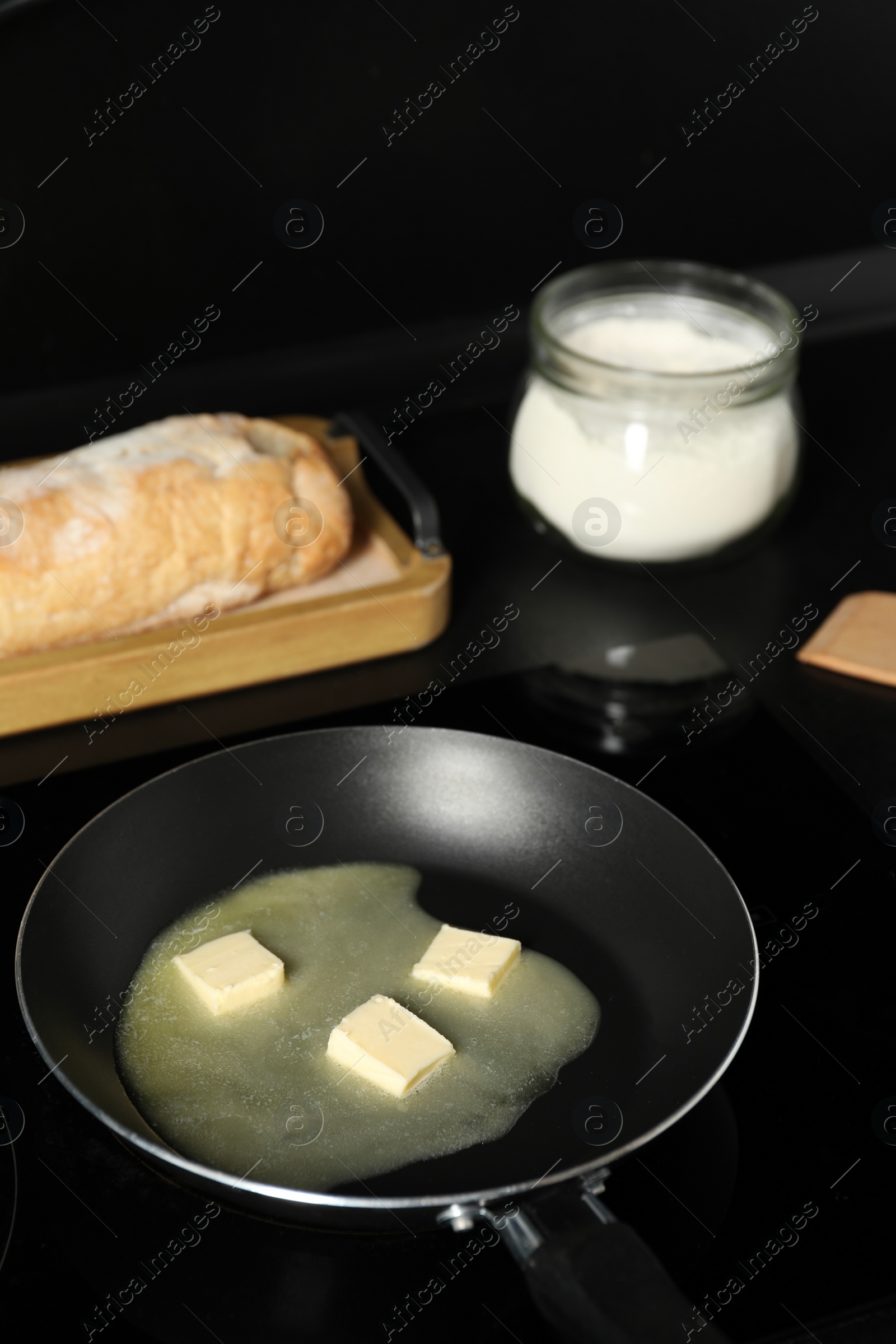 Photo of Melting butter in frying pan, bread and flour on black table