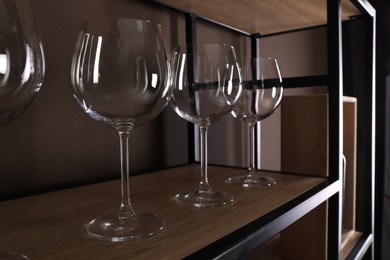 Empty wine glasses on wooden shelf near brown wall