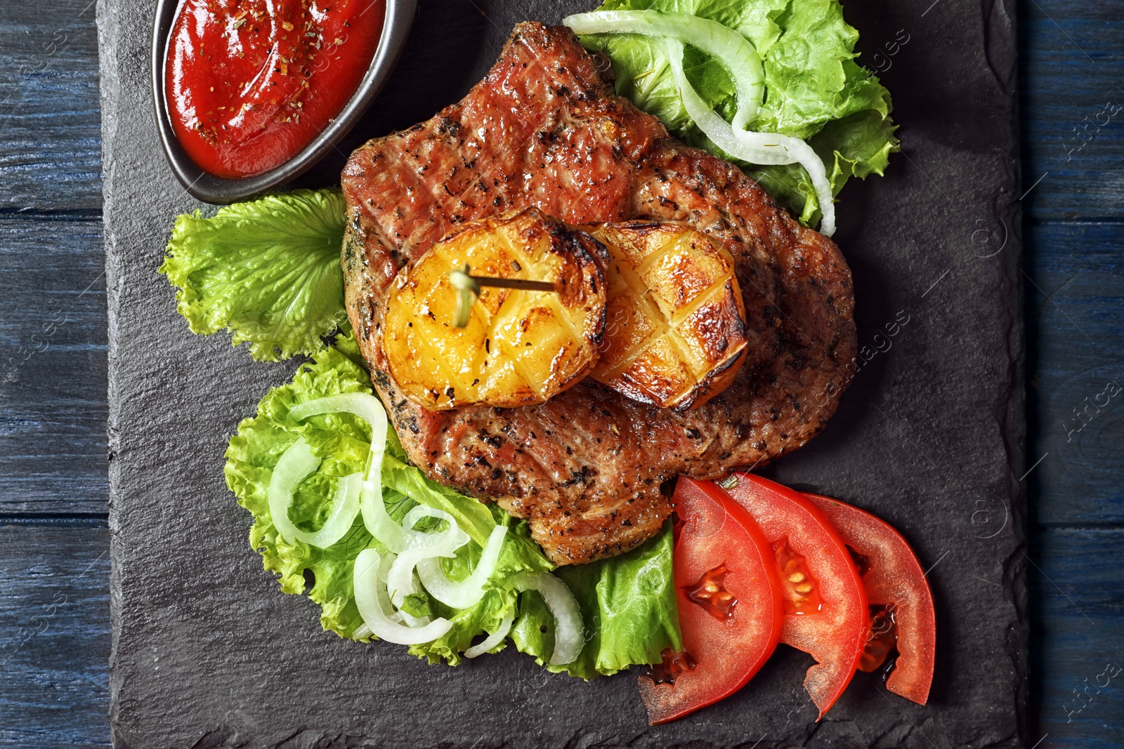 Photo of Slate plate with tasty grilled meat, potatoes and sauce on table, top view